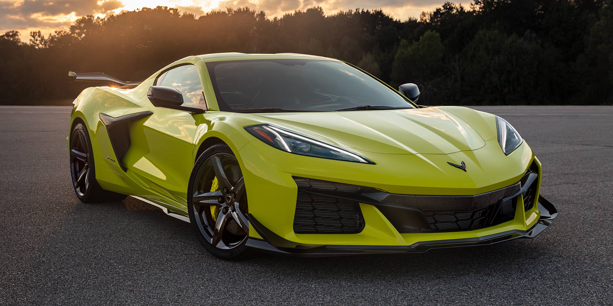 A Lime Green Chevrolet Corvette Z06 Driving on a Curved Road at Sunset with Prominent Aerodynamic Features.