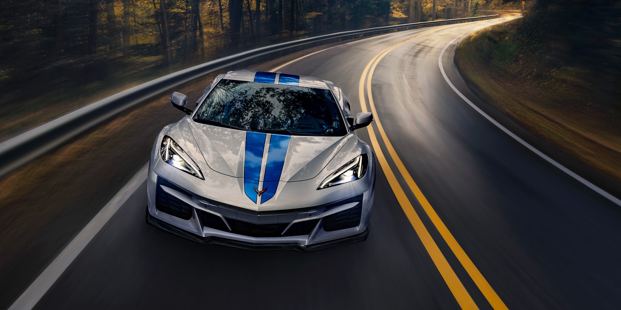 A White Chevrolet Corvette Z06 with Blue Racing Stripes Driving on a Winding Forest Road.