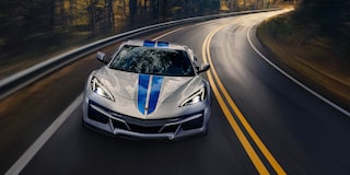 A White Chevrolet Corvette Z06 with Blue Racing Stripes Driving on a Winding Forest Road.