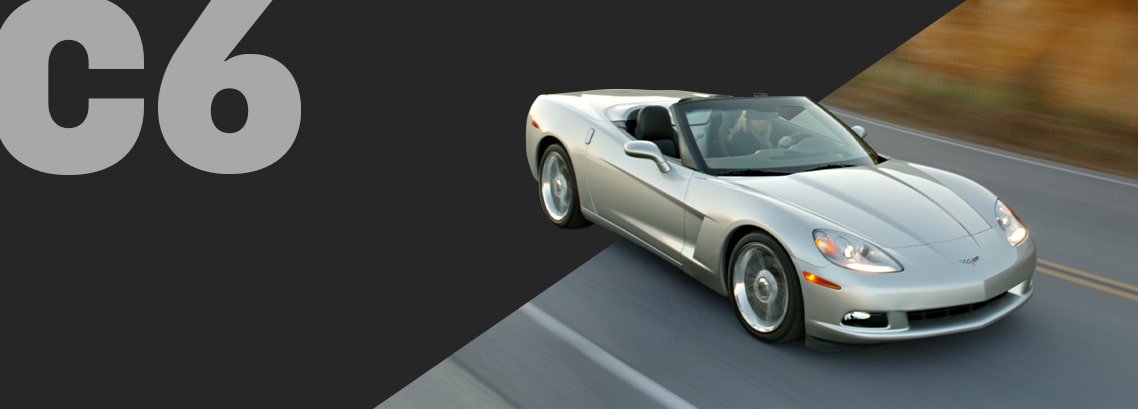 A Silver Chevrolet Corvette C6 Convertible Driving on a Road With a Brown Landscape in the Background and Large Gray Text Reading “C6.”