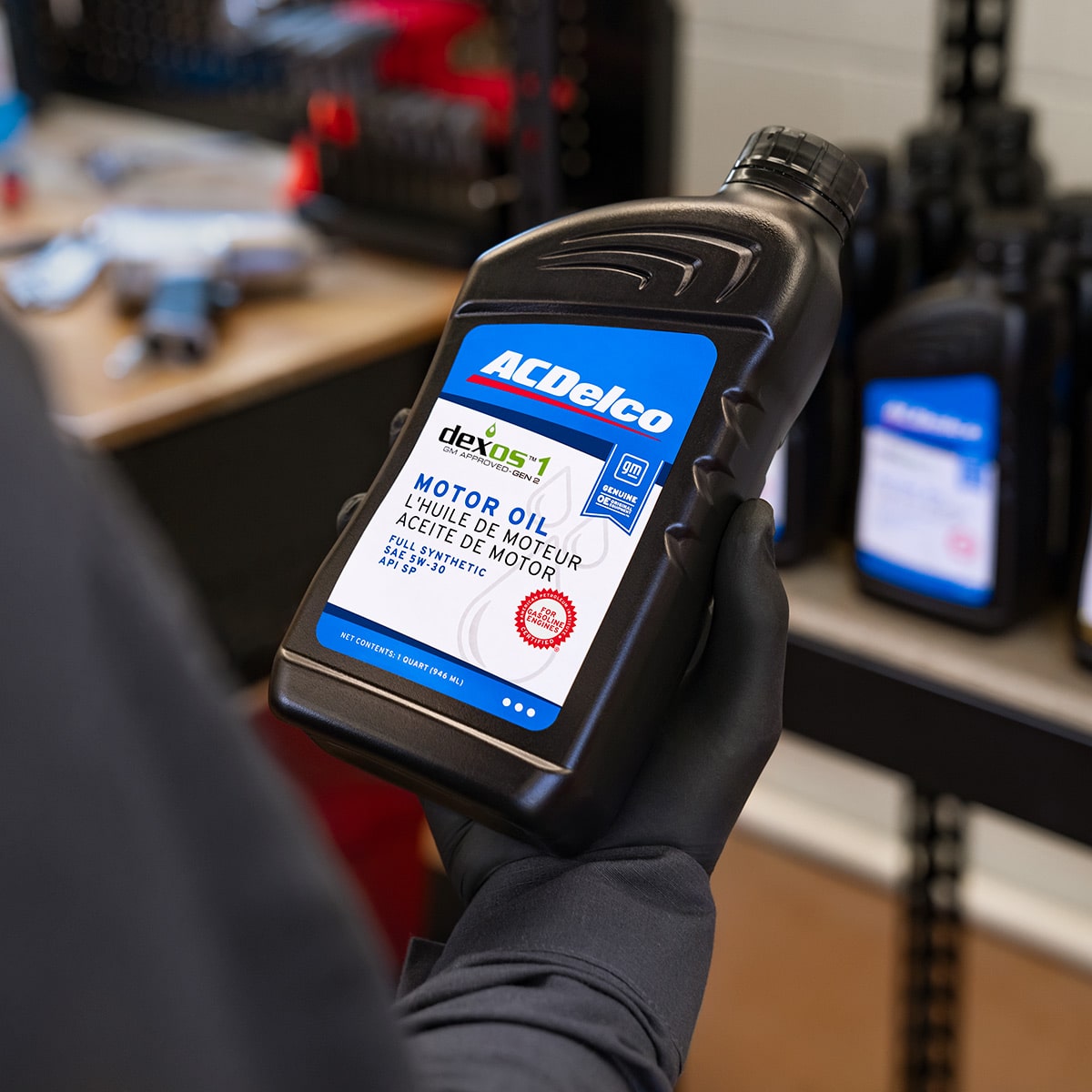 A Person Holding a Black Bottle of ACDelco Motor Oil with Shelves of Automotive Fluids in the Background and Visible Text That Reads Oil, Fluids & Lubricants.