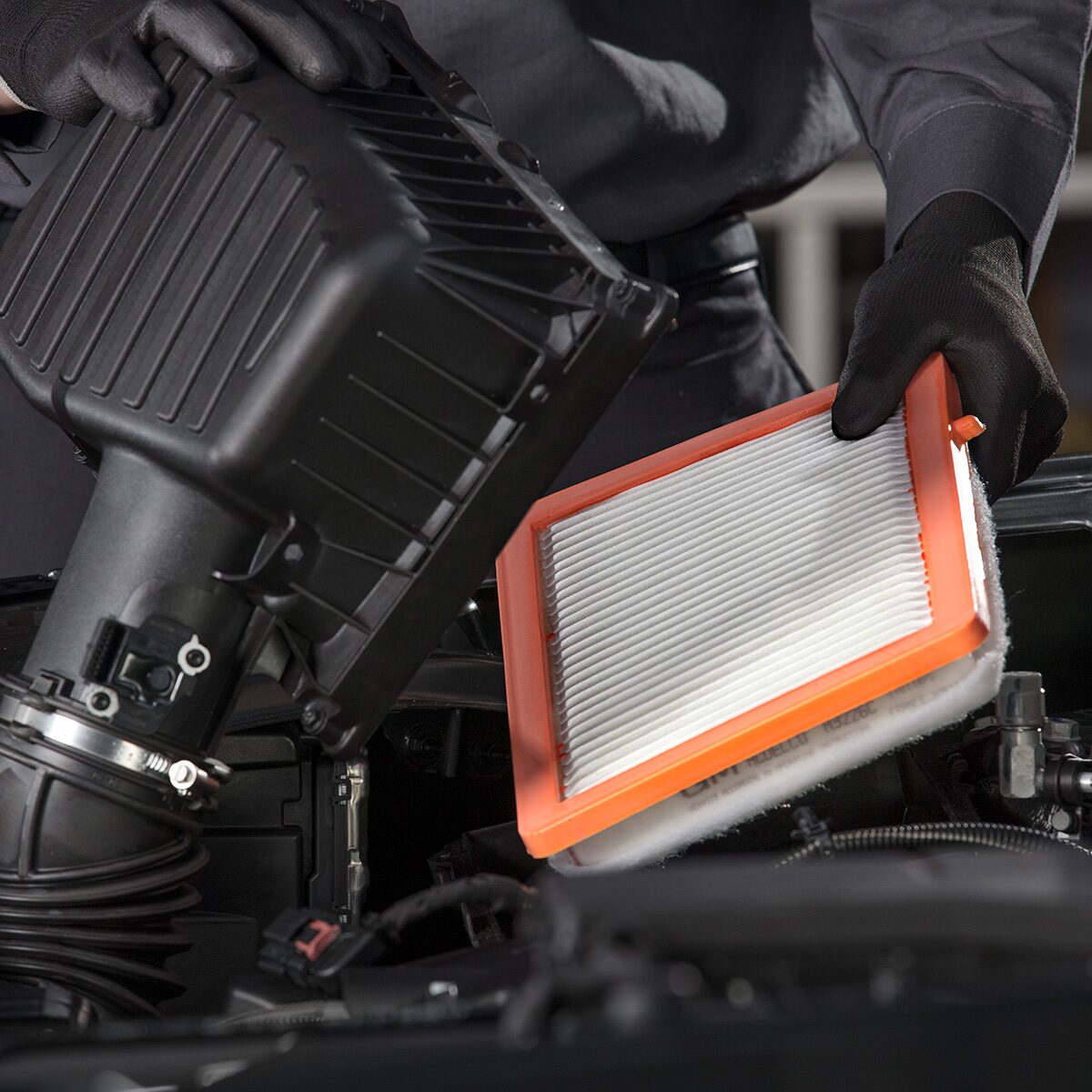 A Person Installing an Orange Automotive Air Filter Inside an Engine Bay with Visible Text That Reads Filters.