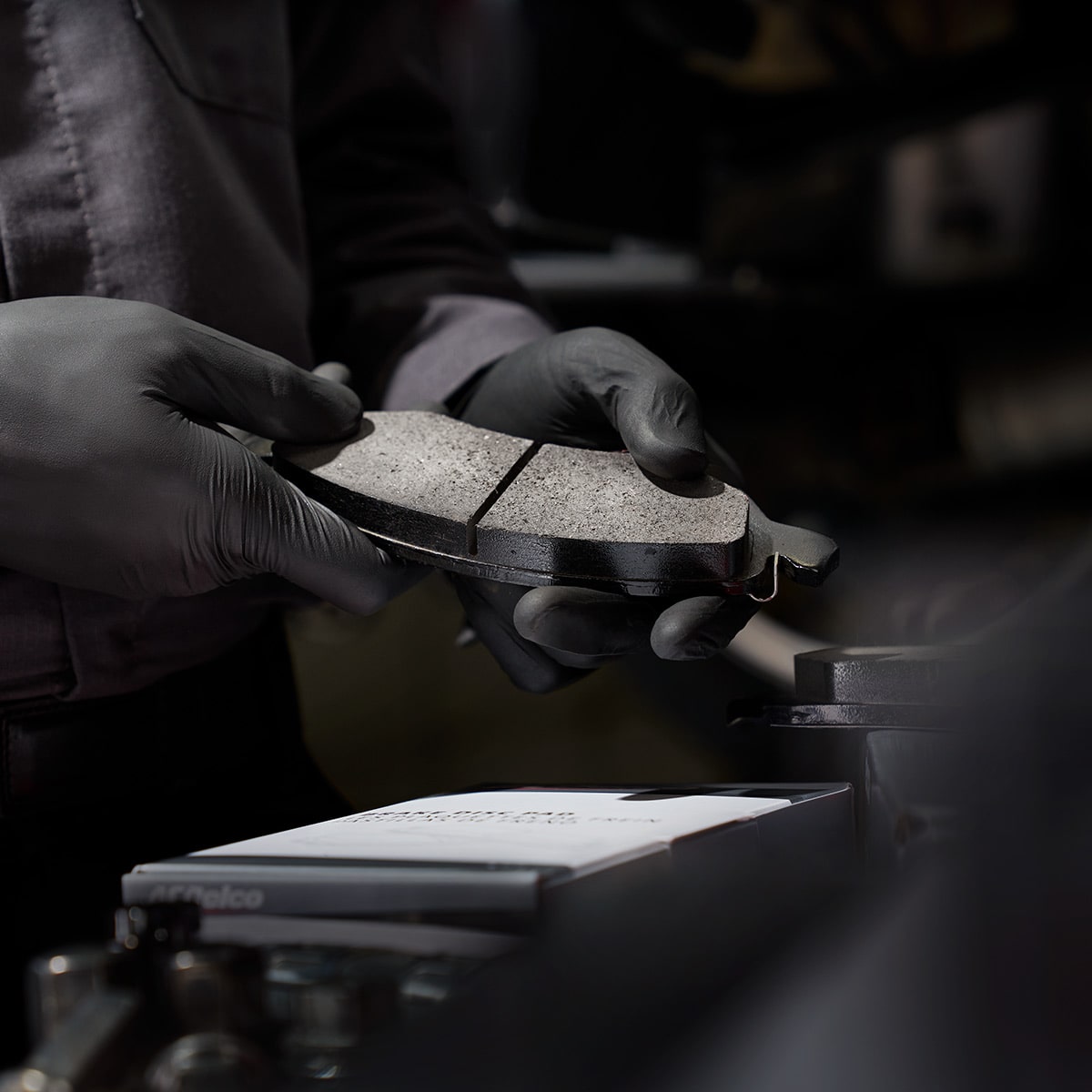 A Person Holding a Brake Pad Over a Workbench with the Word Brakes Displayed in White Text.