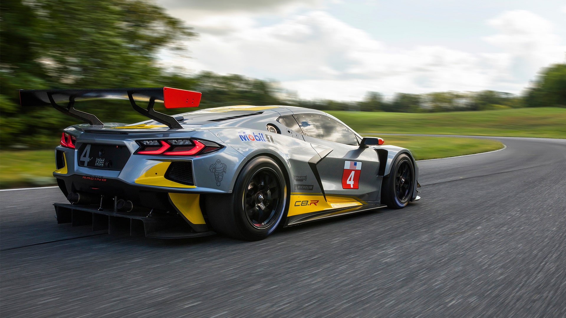 A Rear View of a Black Chevrolet Corvette C7.R Race Car with Yellow Accents Driving on a Road.