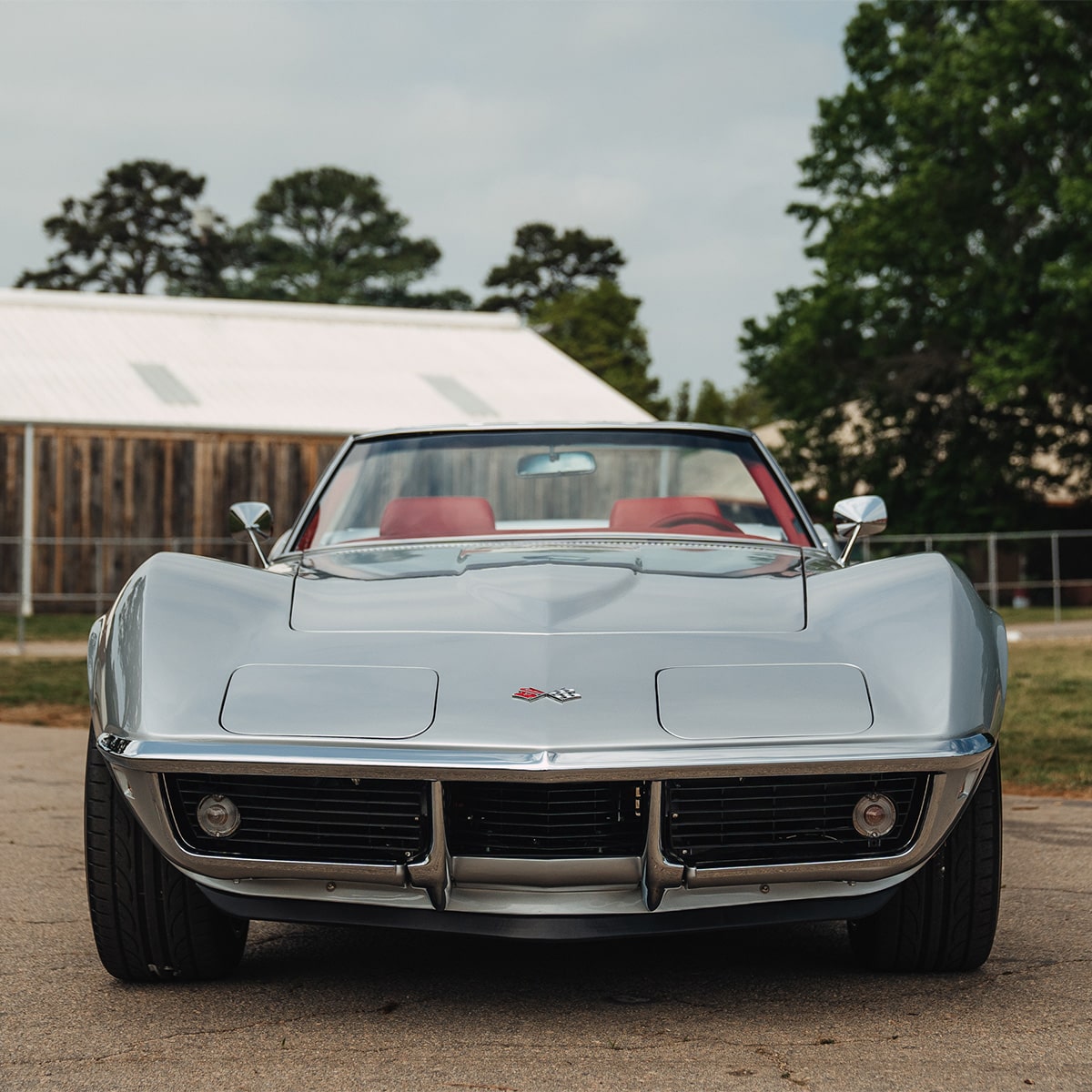 A Front View of a Silver Classic Chevrolet Corvette with Pop-Up Headlights and Chrome Accents Parked Outdoors.