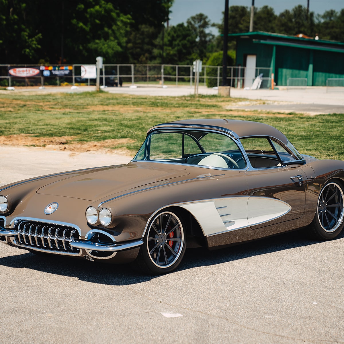 A Side View of a Two-Tone Brown and White Classic Chevrolet Corvette Convertible with Chrome Trim and Polished Wheels Parked Outdoors.