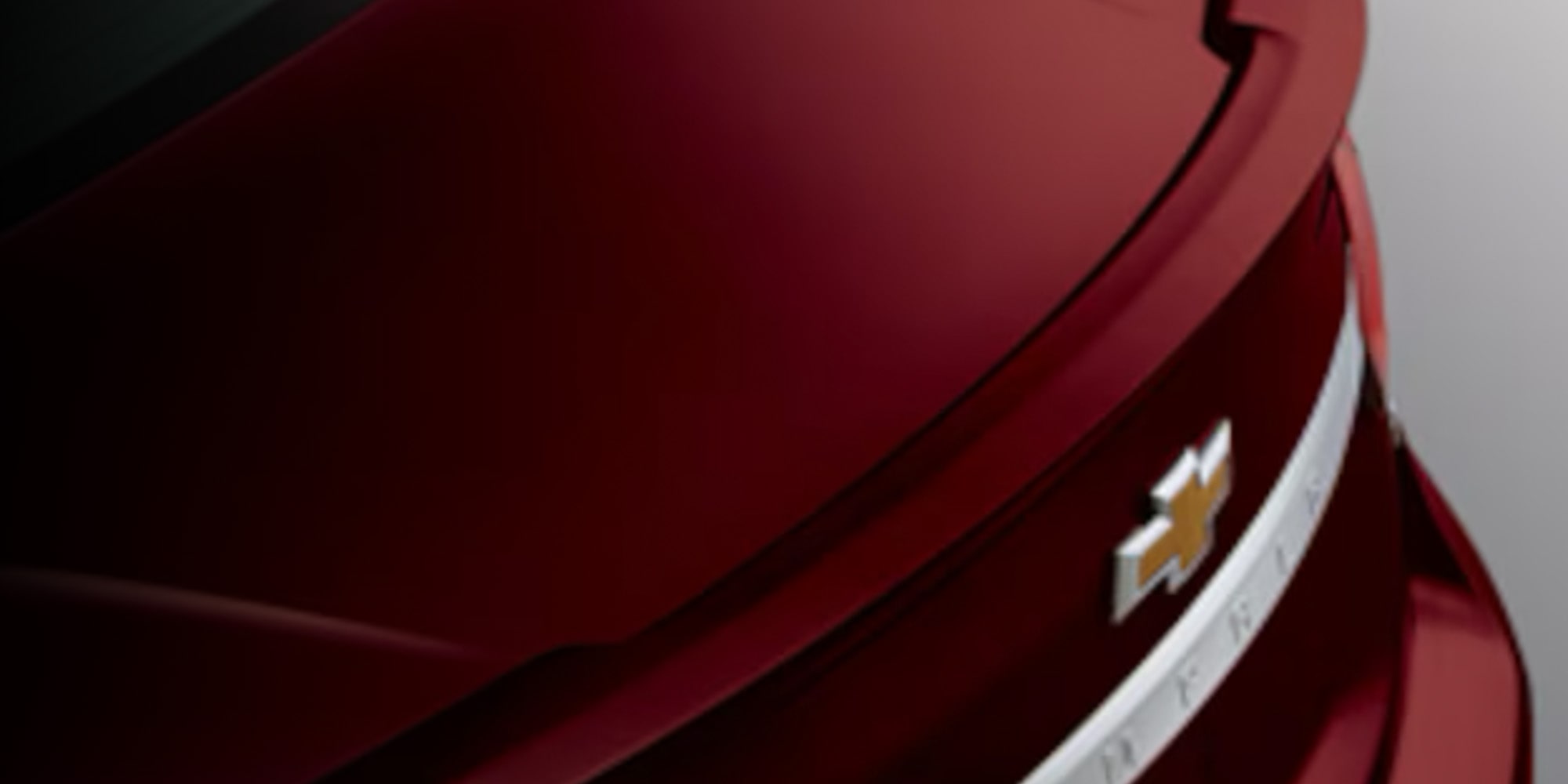 Primer plano de un spoiler trasero de Chevrolet rojo con acabado brillante y moldura cromada, con un fondo negro.