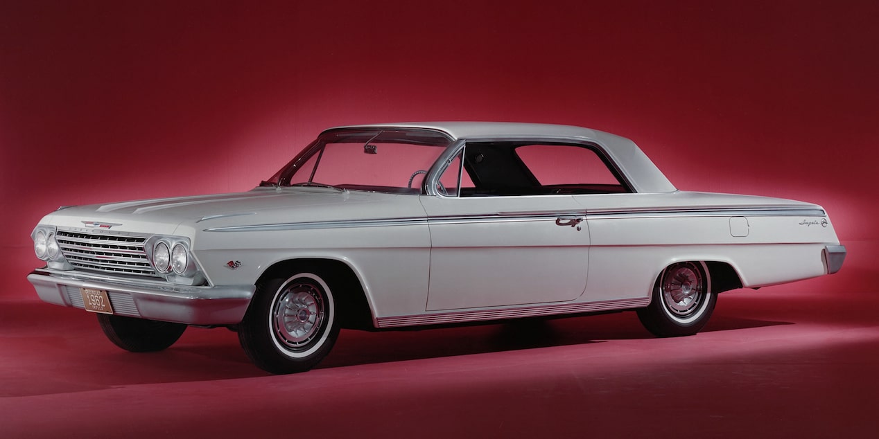 Chevrolet Impala clásico verde claro estacionado frente a una casa, con plantas y un porche cubierto.