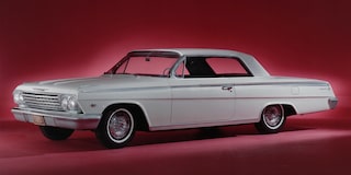 Chevrolet Impala clásico verde claro estacionado frente a una casa, con plantas y un porche cubierto.