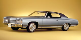 Chevrolet Impala plateado de perfil sobre un fondo amarillo brillante.