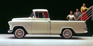 A Classic Cream Chevrolet Silverado 1500 Pickup Truck Parked on a Road With a Person Standing Beside It and Trees in the Background.