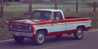 A Red and White Chevrolet Silverado 1500 Pickup Truck Driving on a Rural Road With Grass and Trees in the Background.