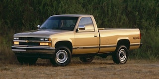 A Gold Chevrolet Silverado 1500 Pickup Truck Parked on a Dirt Road With Green Trees in the Background.
