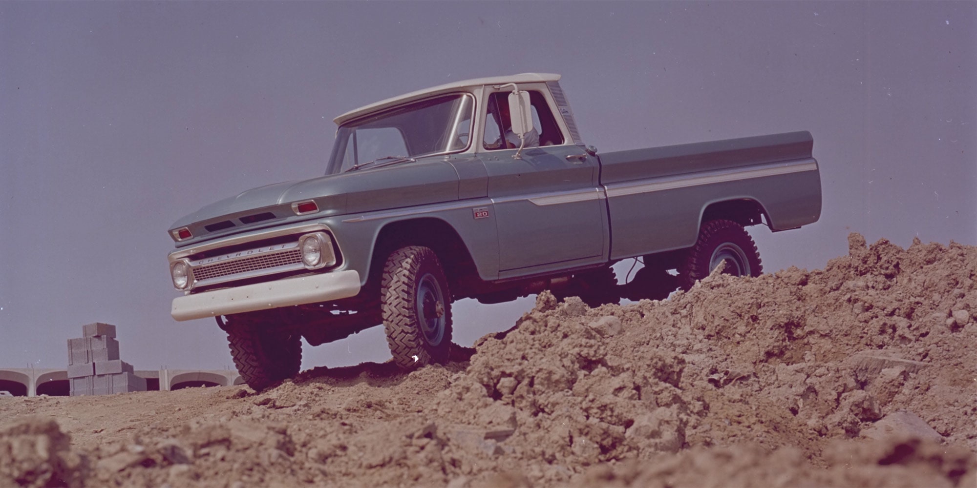 A Gray Chevrolet Silverado 1500 Pickup Truck Parked on a Dirt Road With a Purple Sky and Trees in the Background.
