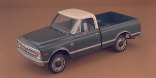 A Teal Chevrolet Silverado 1500 Pickup Truck Parked on a Road With a White Roof and Chrome Accents Against a Brown Landscape.