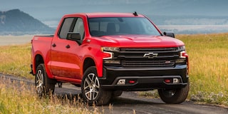 A Red Chevrolet Silverado 1500 LT Trail Boss Parked on a Grassy Field With Mountains and a Clear Sky in the Background.