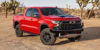 A Red Chevrolet Silverado 1500 ZR2 Parked on a Dirt Surface With Desert Vegetation and Trees in the Background.