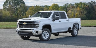 A White Chevrolet Silverado EV Parked on a Gravel Road With a Modern Building and Trees in the Background.