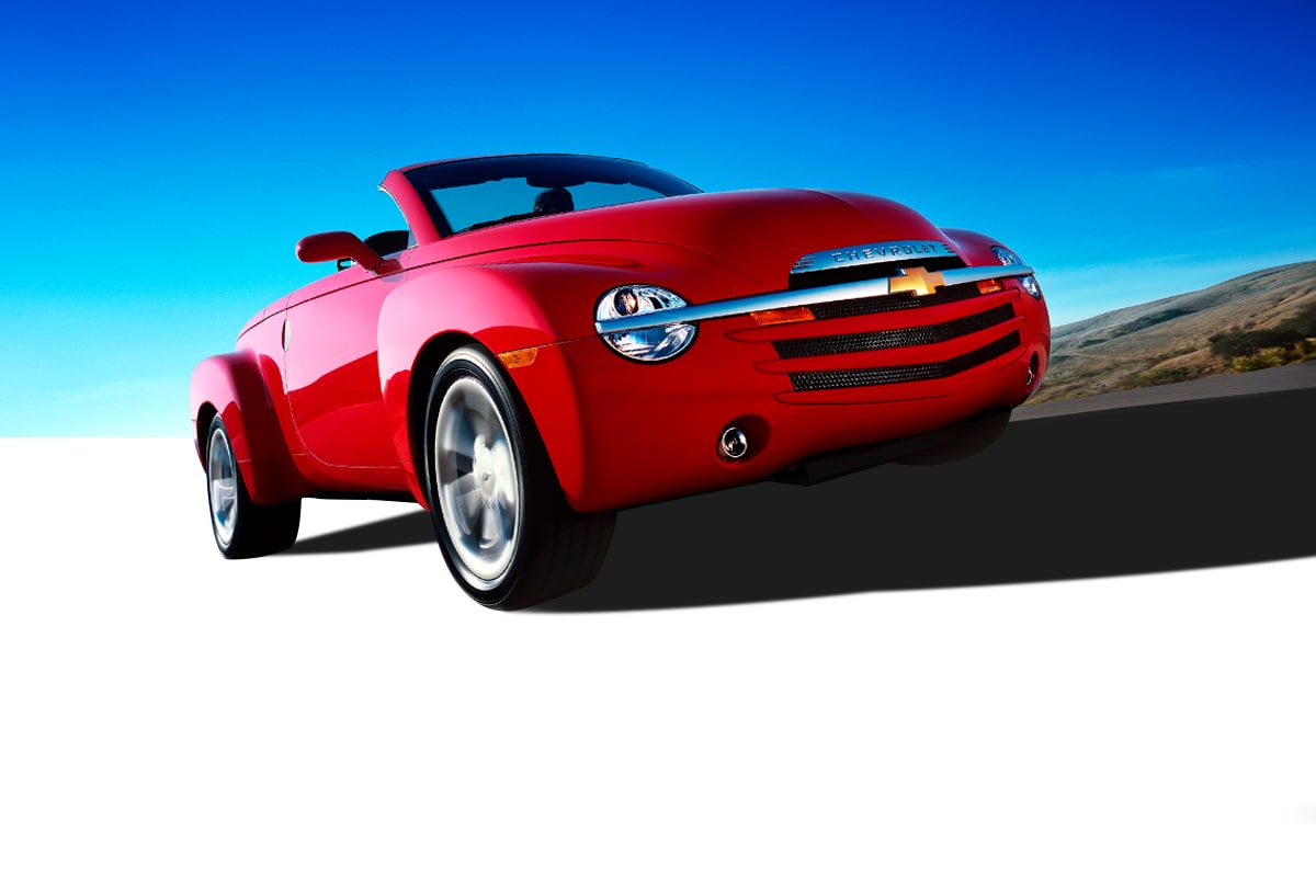 Red Chevrolet Convertible Vehicle Driving on a Road under a Bright Blue Sky with a Front Low-Angle View.