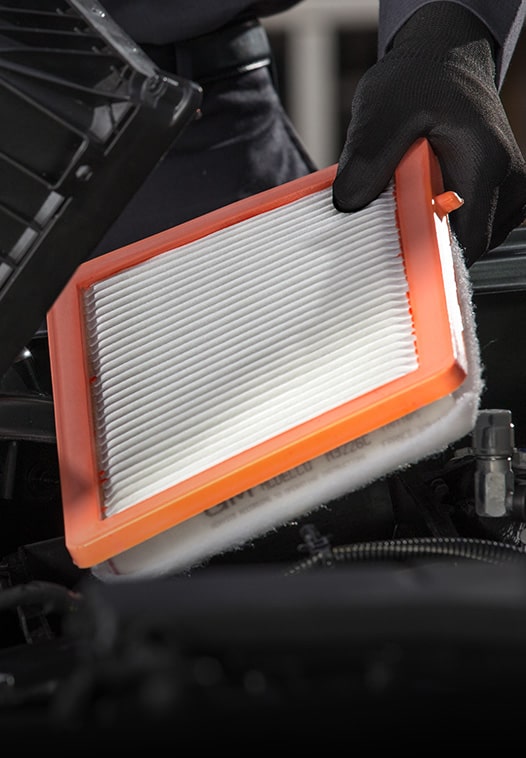 Gloved Technician Holding a Rectangular Orange-Framed Engine Air Filter Under an Open Hood