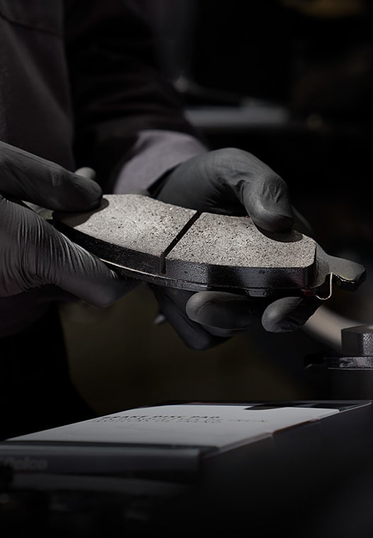 Mechanic Wearing Gloves Holding a Pair of New Brake Pads Under a Spotlight