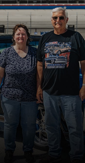A Woman and a Man Stand in Front of a Racetrack