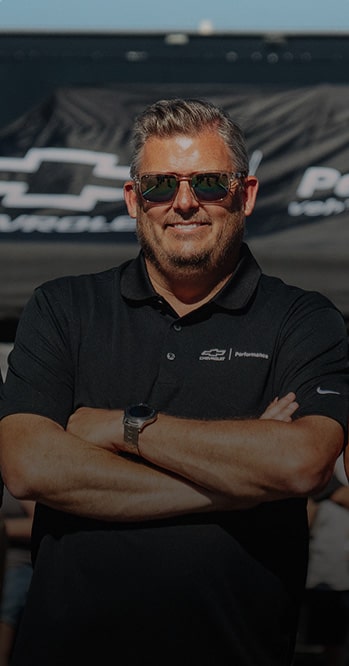 A Man Wearing Sunglasses with Arms Crossed Stands in Front of a Chevy Tent