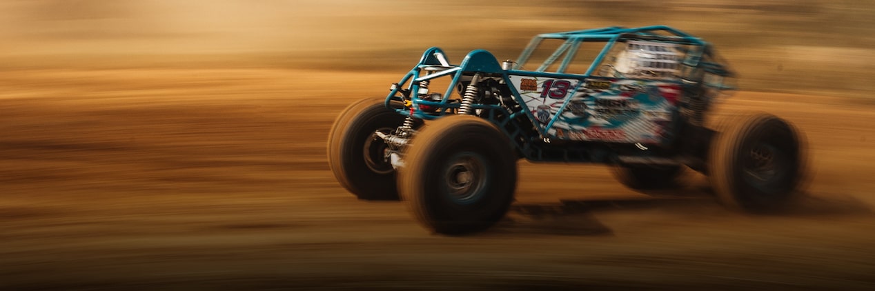 A Blue and Black Off-Road Buggy with an Exposed Roll Cage Races Across a Dirt Trail, with Motion Blur in the Background Emphasizing Speed.