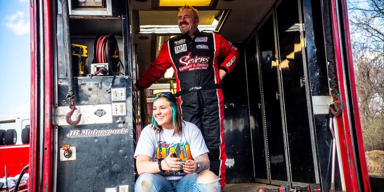 A Race Car Driver Standing Next to His Daughter Who is Sitting in Front of a Shop