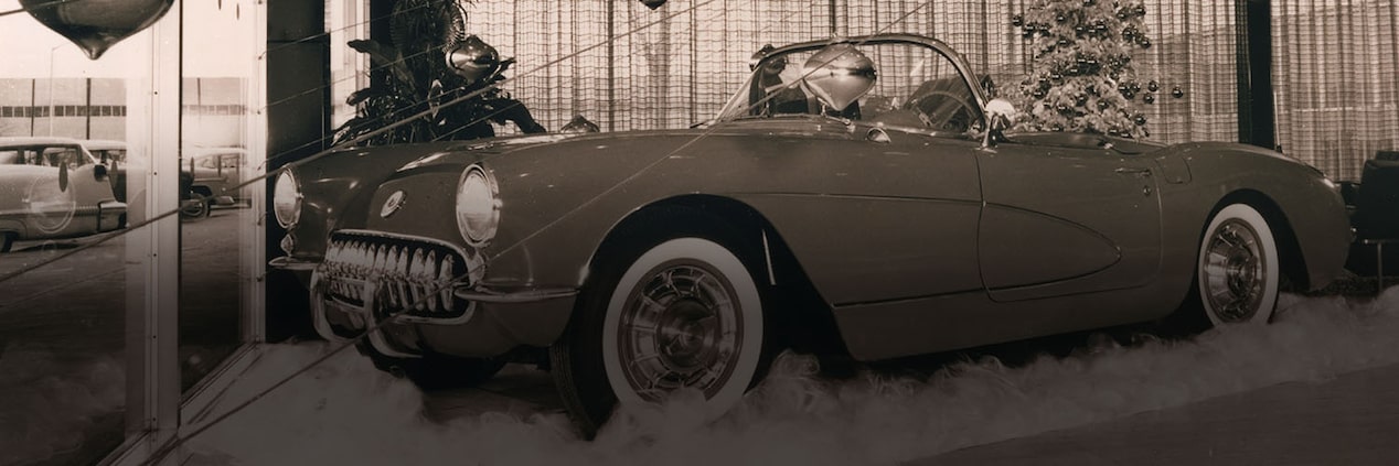 A Black and White Photo of a Vintage Chevrolet Convertible Parked on a Rug in a Display Room with Ornaments on the Ceiling and a Christmas Tree in the Background