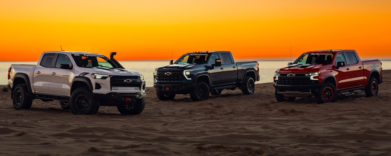 Three Chevrolet Pickup Trucks Parked on a Scenic Beach with a Beautiful Sunset in the Distance