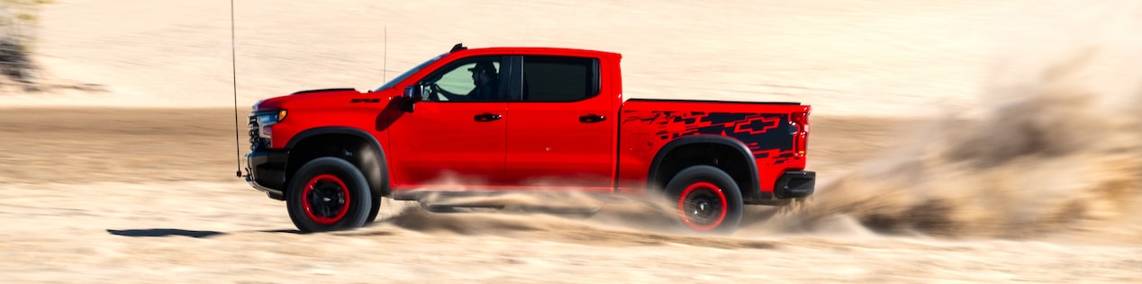 A Distant Side View of a Red Chevrolet Silverado Driving in a Desert with a Cloudy Sky Overhead