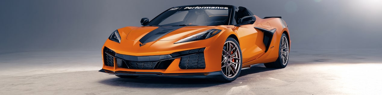Front Three Quarters View of an Orange Chevrolet Corvette Parked on Concrete with a Grey Background