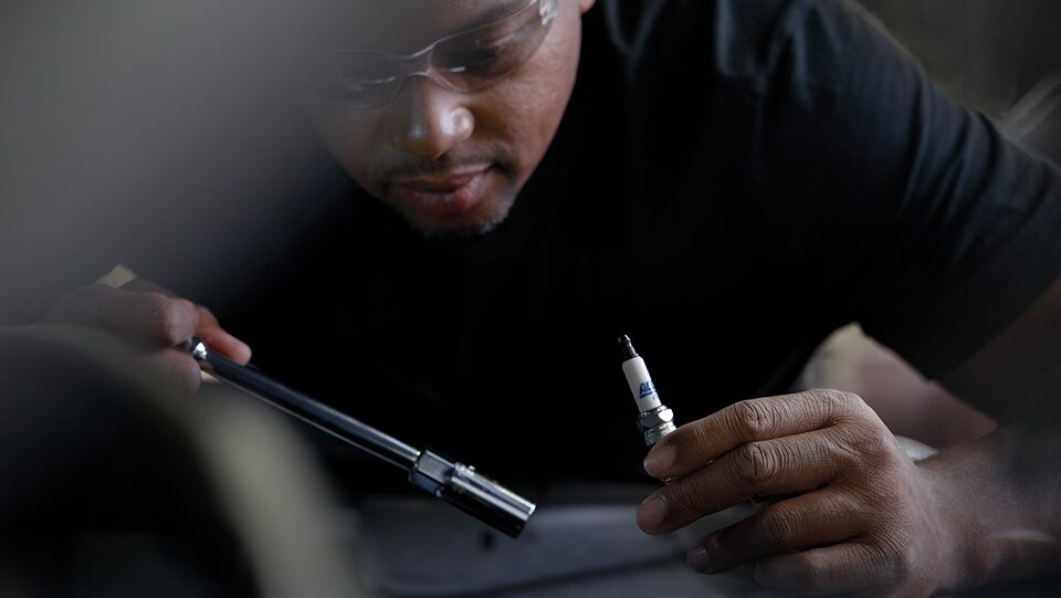 A Technician Holding a Spark Plug and Tools While Inspecting a Vehicle