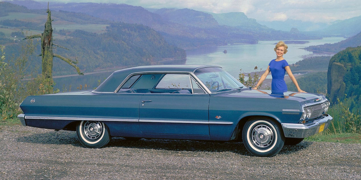 Side View of a Blue 1963 Chevy Impala SS Parked on a Rural Road with a Woman in a Blue Dress Standing Near the Hood