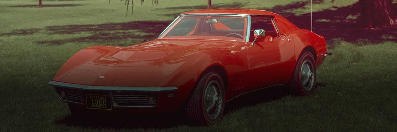 A Vintage Red Chevrolet Sports Car Parked on Lush Green Grass Near a Massive Tree Casting Shade in the Backgrouund