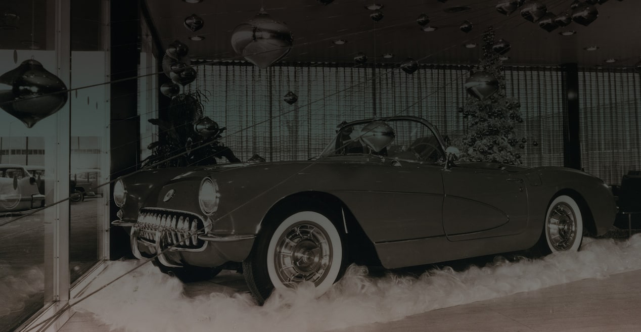 A Black and White Photo of a Vintage Chevrolet Convertible Parked on a Rug in a Display Room with Ornaments on the Ceiling and a Christmas Tree in the Background