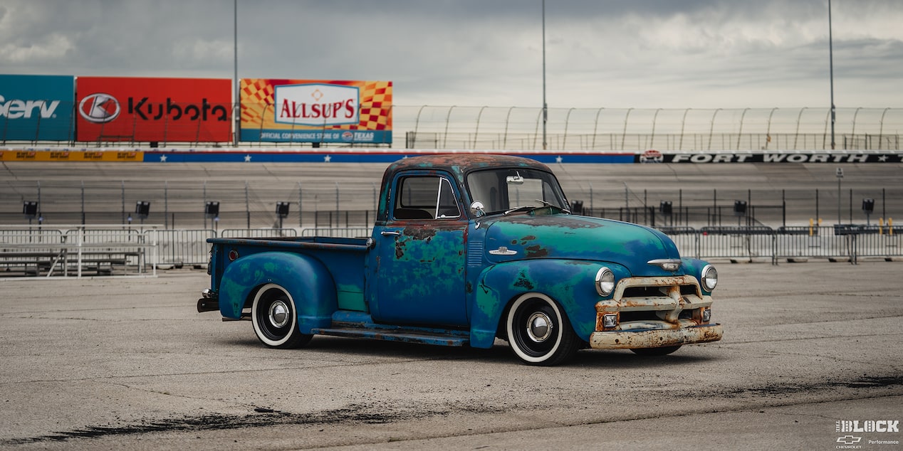 A Blue 1955 Chevy Pickup Truck Parked in Front of a Racetrack