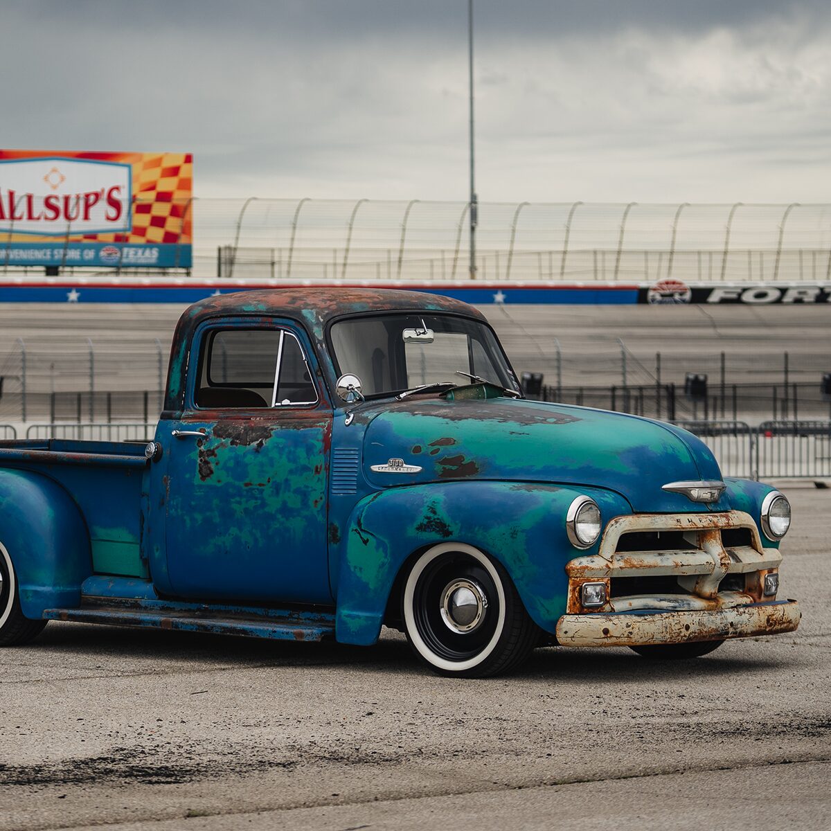 A Blue 1955 Chevy Pickup Truck Parked in Front of a Racetrack
