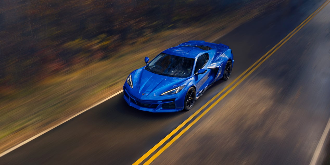 Un Chevy deportivo en Azul Oscuro avanza por una carretera rural rodeada de bosque