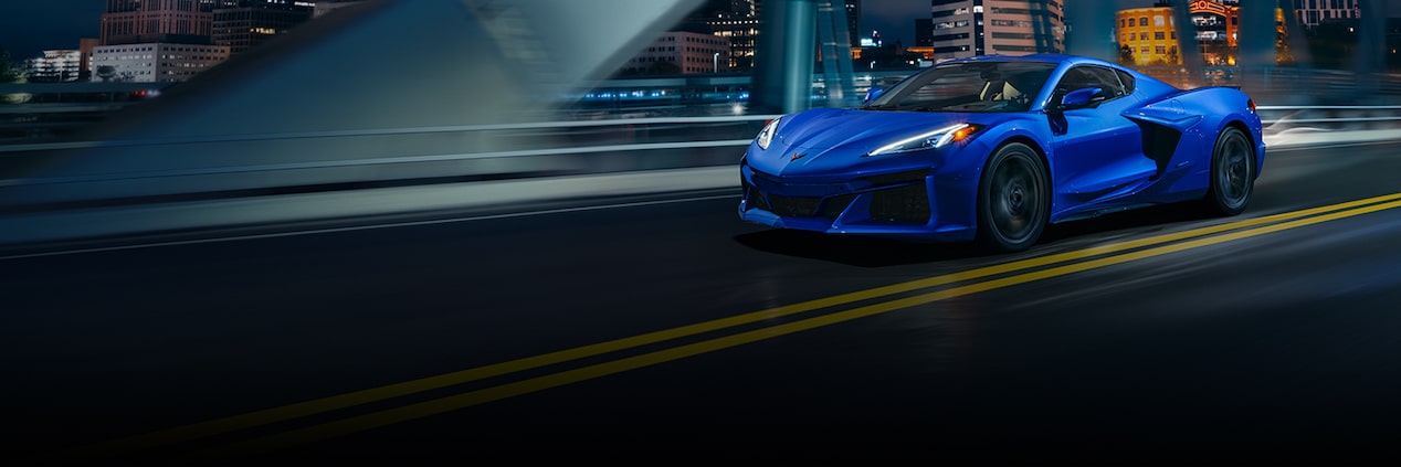 Un Chevrolet deportivo Azul Oscuro circula de noche por el puente de una ciudad con un horizonte lleno de rascacielos