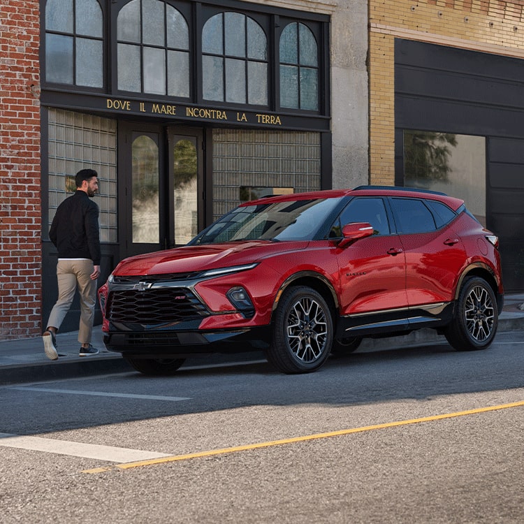 Man Walking Toward His 2026 Red Chevy Blazer Parked at a Shop