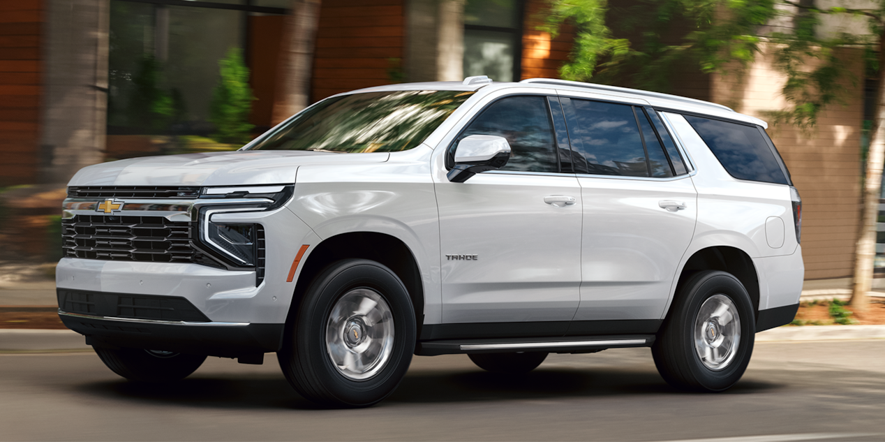 Profile View of a White 2026 Chevy Tahoe SUV Driving Past a Brick Building