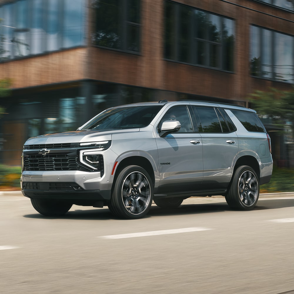 A 2026 Chevrolet Tahoe Driving Past a Modern Building in an Urban Setting on a Bright Day.