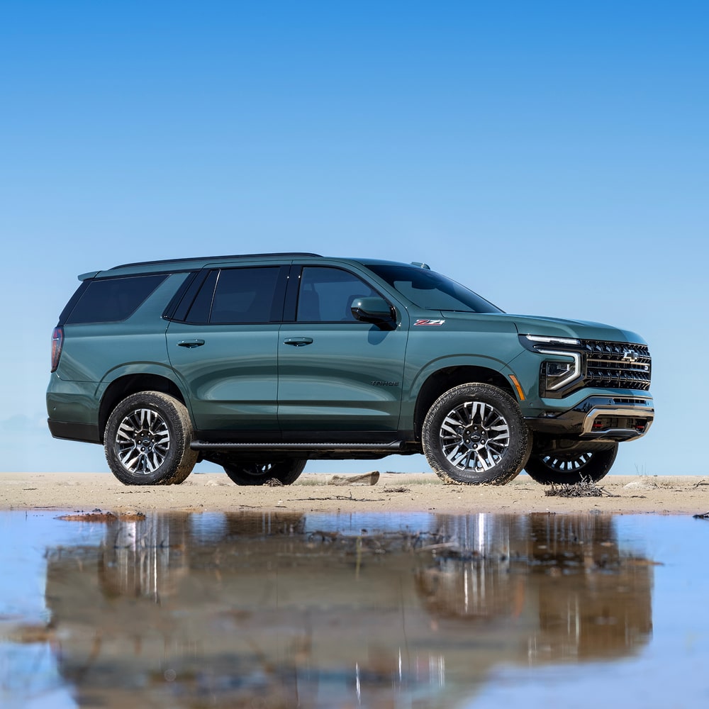 A 2026 Chevrolet Tahoe Reflected in a Shallow Pool of Water While Parked on a Flat, Sunlit Surface Beneath a Clear Blue Sky.
