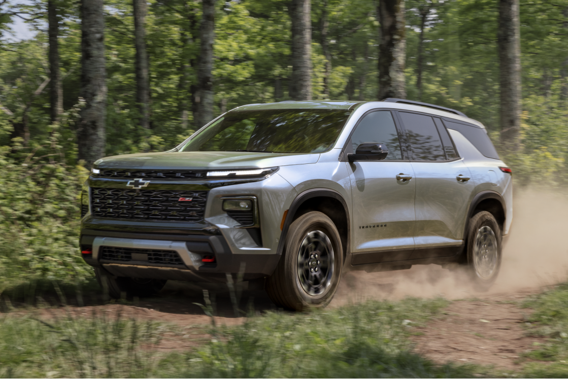 A 2027 Chevy Traverse Driving on a Dirt Trail Through a Forested Landscape.