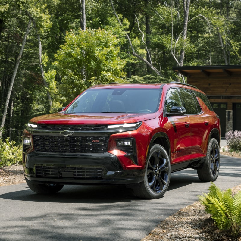 A 2027 Chevy Traverse Parked Outside a Cabin Surrounded by Trees and Natural Scenery.