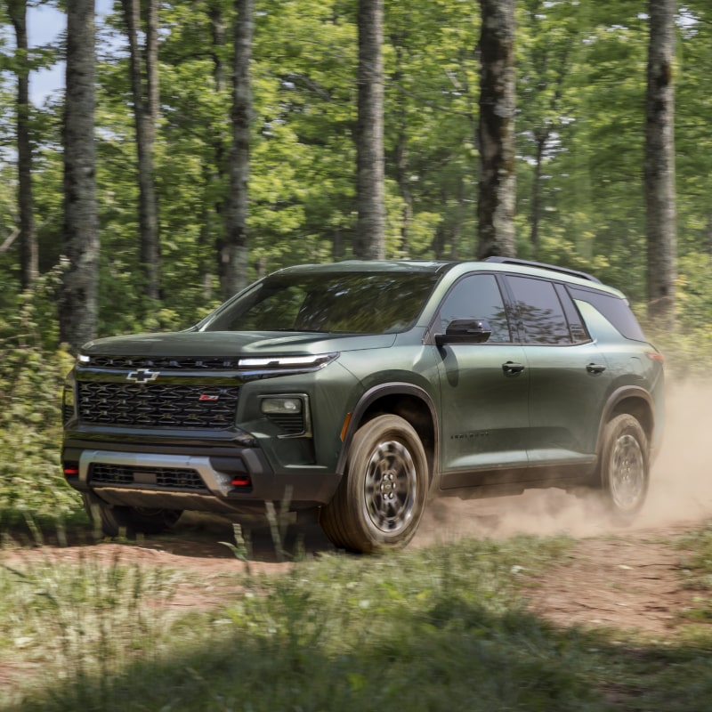 A 2027 Chevy Traverse Driving on a Dirt Trail Through a Forested Landscape.