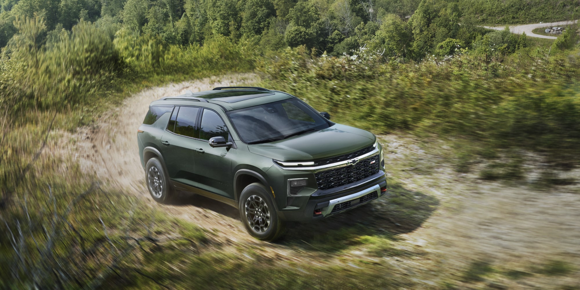 A 2027 Chevy Traverse Driving Along a Dirt Road Through a Natural Landscape Showcasing Rugged SUV Styling and Adventure-Ready Capability.