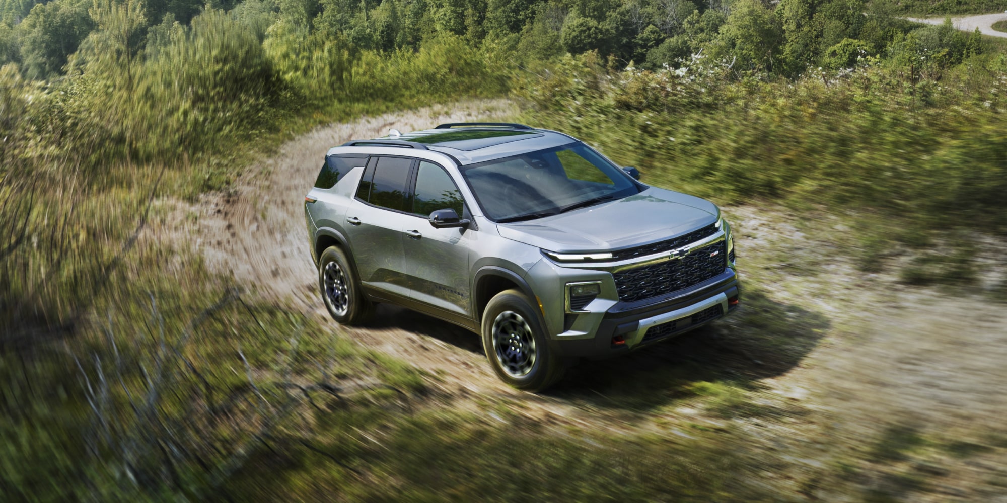 A 2027 Chevy Traverse Driving Along a Dirt Road Through a Natural Landscape Showcasing Rugged SUV Styling and Adventure-Ready Capability.